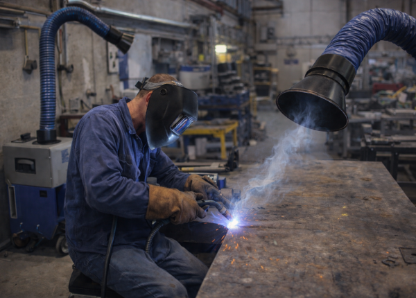 Welder working in a compact fabrication shop with a welding fume extractor capturing fumes at the source.